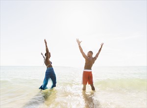 Mature couple standing in sea with arms raised