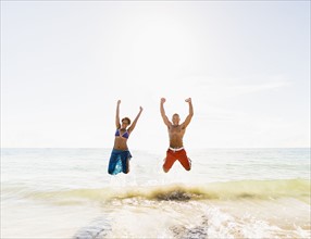 Mature couple jumping in sea with arms raised