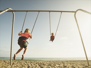 Girl (4-5) and boy (2-3) swinging on beach