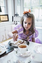 Girl (4-5) eating cookies at dining table
