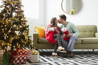 Young couple with Christmas stockings kissing on sofa