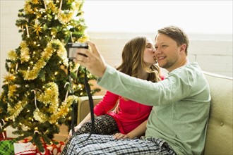 Young couple taking selfie on sofa at Christmas