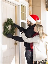 Young couple hanging wreath on door