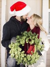Young couple holding wreath, looking face to face
