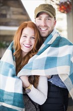 Portrait of mid adult couple wrapped in checked blanket