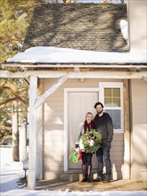 Young couple holding wreath standing in front of house