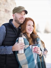 Mid adult couple having drink from vacuum flask, looking away