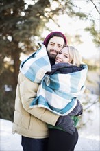 Couple wrapped in blanket hugging outdoors