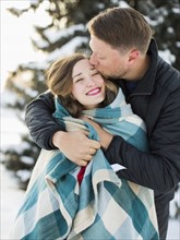 Man kissing woman wrapped in blanket outdoors