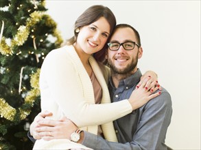 Studio portrait of couple embracing in front of Christmas tree