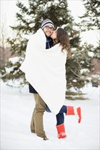 Couple wrapped in blanket standing in snow