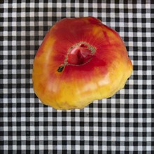 Heirloom tomato on checkered tablecloth.