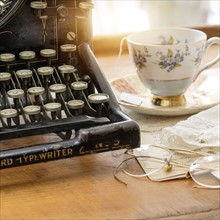 Studio shot of antique typewriter with teacup and eyeglasses.