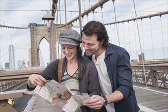 Happy couple reading map on Brooklyn Bridge. Brooklyn, New York.
