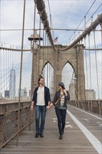 Couple holding hands and walking on Brooklyn Bridge. Brooklyn, New York.