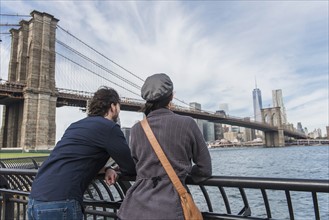 Couple leaning against railing and looking at Freedom Tower. Brooklyn, New York.