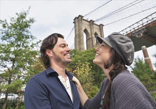 Happy couple standing against Brooklyn Bridge. Brooklyn, New York.