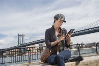 Woman using tablet pc, Manhattan Bridge in background. Brooklyn, New York.