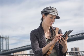Woman using tablet pc, Manhattan Bridge in background. Brooklyn, New York.