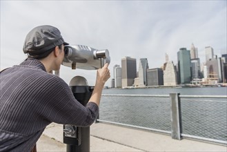 Woman watching cityscape through coin-operated binoculars. Brooklyn, New York.