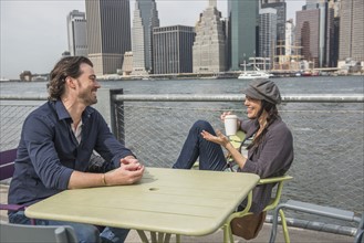Happy couple sitting and discussing with cityscape in background. Brooklyn, New York.