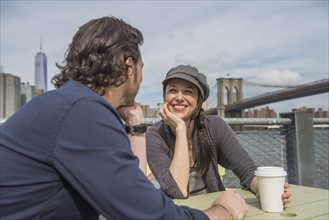 Happy couple sitting and discussing with cityscape in background. Brooklyn, New York.
