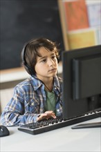 Schoolboy (6-7) using computer in classroom.