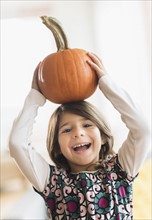 Portrait of happy girl (6-7) with pumpkin on head.