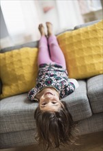 Girl (6-7) lying upside down on sofa.