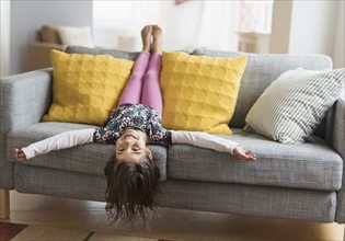 Girl (6-7) lying upside down on sofa.