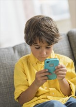 Boy (6-7) sitting on sofa and using cell phone.