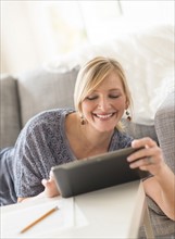 Smiling woman lying down on sofa with tablet pc.