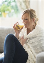 Woman sitting on sofa and drinking orange juice.