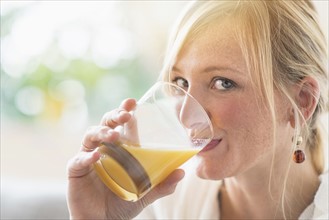 Woman sitting in living room and drinking orange juice.