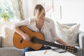 Woman sitting on sofa and playing acoustic guitar.