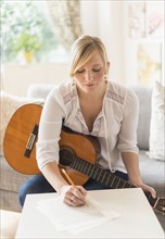 Woman sitting on sofa with acoustic guitar and writing.