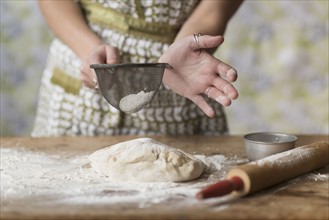 Woman sifting flour while kneading dough.