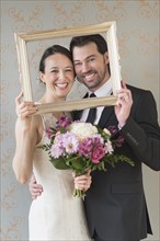 Bride and groom posing with picture frame. .
