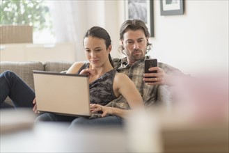 Couple on sofa, woman using laptop and man mobile phone.