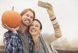 Couple taking selfie with mobile phone, man holding pumpkin.