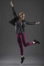 Studio shot of cheerful woman jumping with arms raised.
