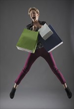 Studio shot of woman jumping with shopping bags.