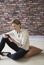 Young woman sitting on floor and using digital tablet.