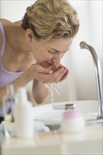 Young woman washing face in bathroom.