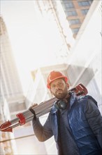 Portrait of construction worker carrying tripod on shoulder.