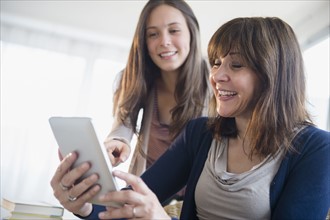 Teenage girl (14-15) using digital tablet with her mom in living room