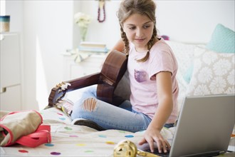 Girl (12-13) playing guitar and using laptop