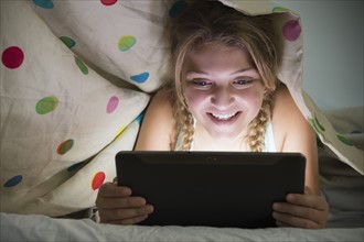 Girl (12-13) using tablet in bed
