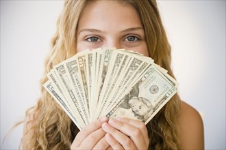 Girl (12-13) holding money fan against her face