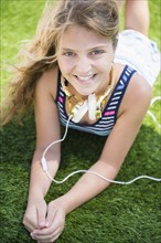 Girl (12-13) lying in grass with headphones